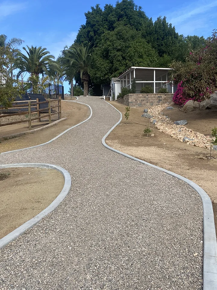 Completed backyard landscape with extruded concrete curbing, dry creek bed, decomposed granite path, and native plantings
